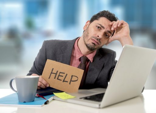 sad businessman at office desk working on computer laptop asking for help depressed